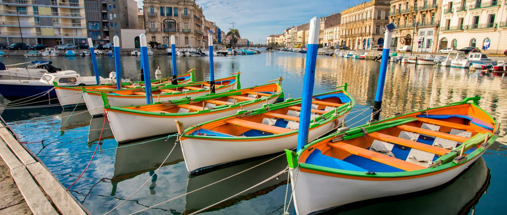 Colorful traditional fishing boats moored in a canal in Sète, France, lined with historic buildings.