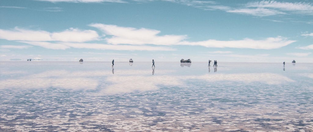 Tourists walking on the reflective Salar de Uyuni salt flats under a blue sky in Bolivia.