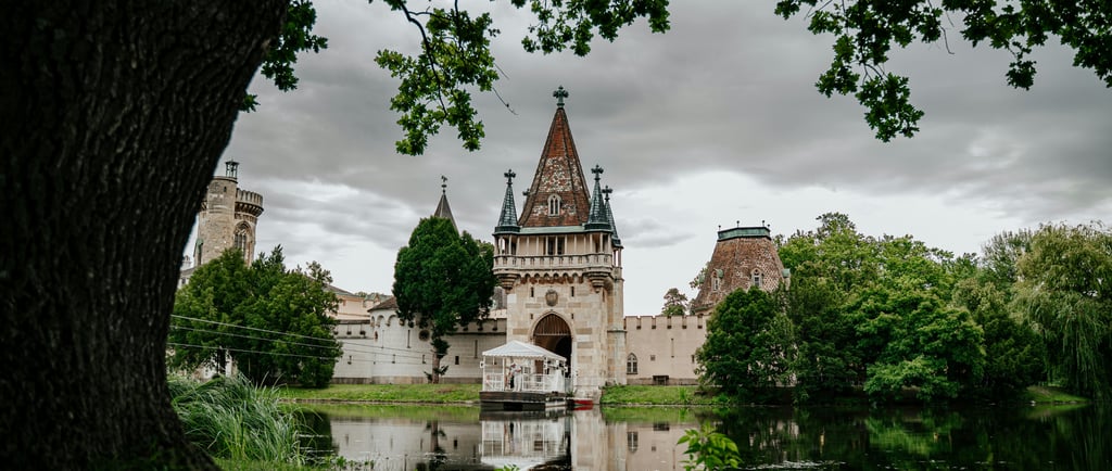Laxenburg Castle Park featuring the historic Franzensburg castle reflected in a calm lake under a cloudy sky.