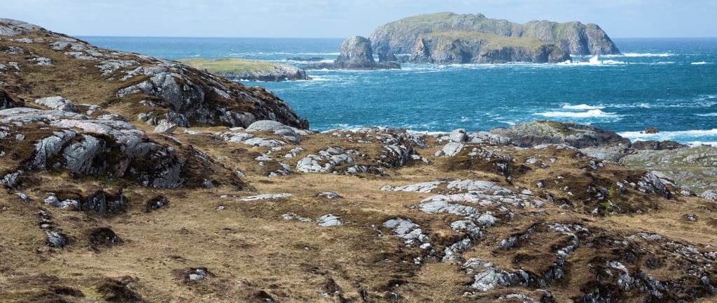Rugged coastal landscape of the Scottish Highlands overlooking the blue Atlantic Ocean and rocky islands.