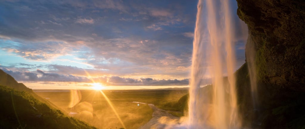 Seljalandsfoss waterfall in Iceland illuminated by a golden sunset with a dramatic sky.