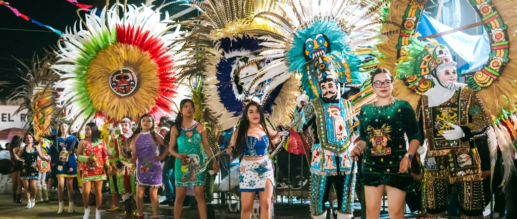 Dancers in colorful traditional costumes and feather headdresses at a vibrant street festival parade.