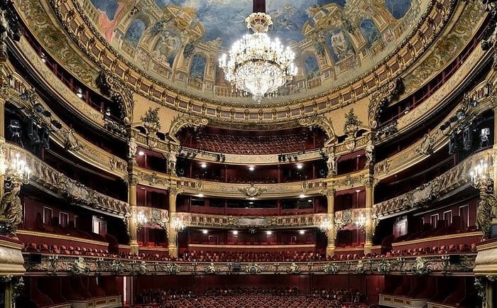 Ornate interior of a historic opera house featuring gold balconies, a painted ceiling, and a crystal chandelier.
