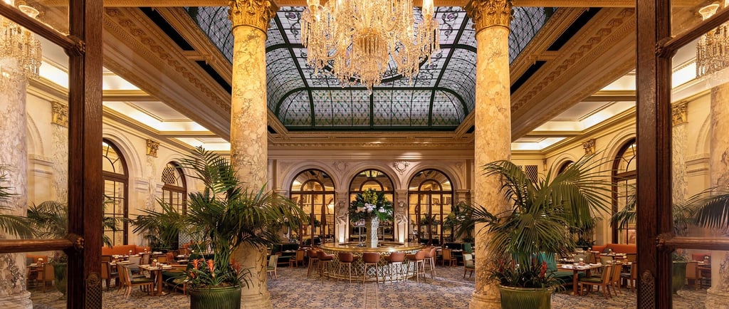 Elegant luxury hotel dining room with crystal chandelier, marble columns, and a stained glass ceiling.
