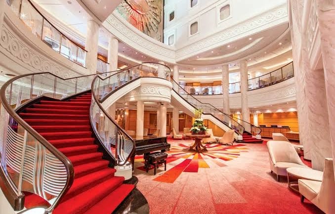 Grand luxury hotel lobby featuring a sweeping red carpet staircase and elegant piano lounge.