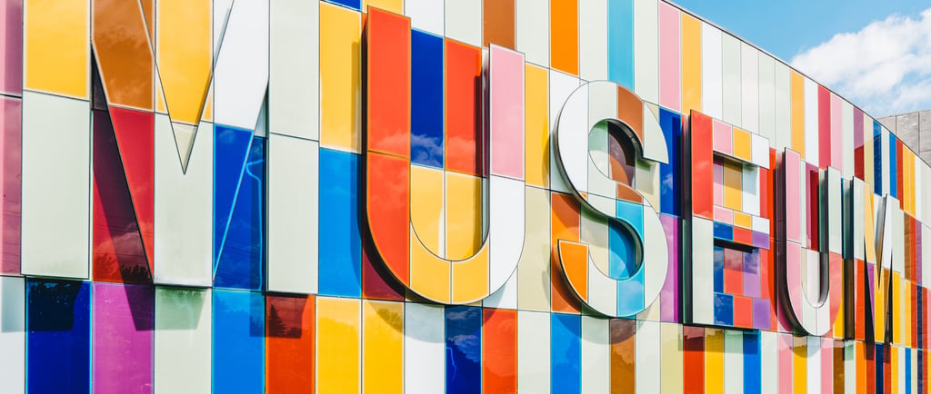 Modern museum building with a vibrant multi-colored glass facade and large 3D museum signage.