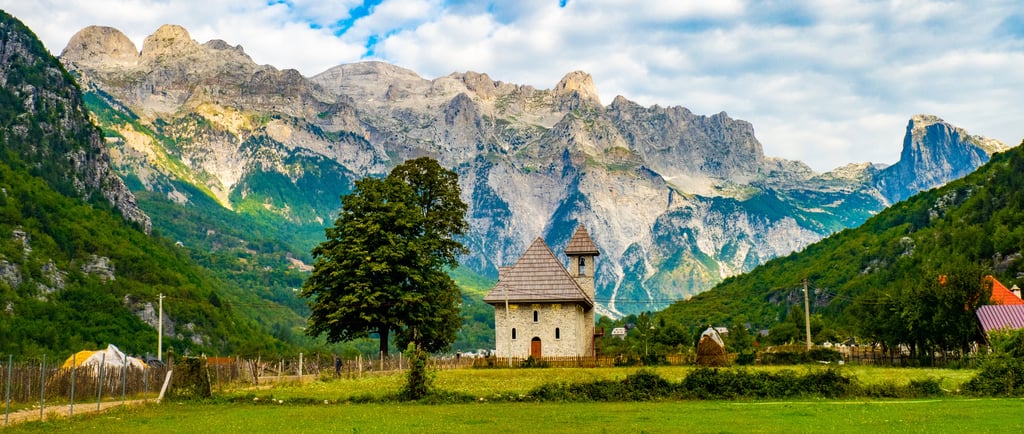 Small stone church in a green meadow with the Accursed Mountains in Theth, Albania.
