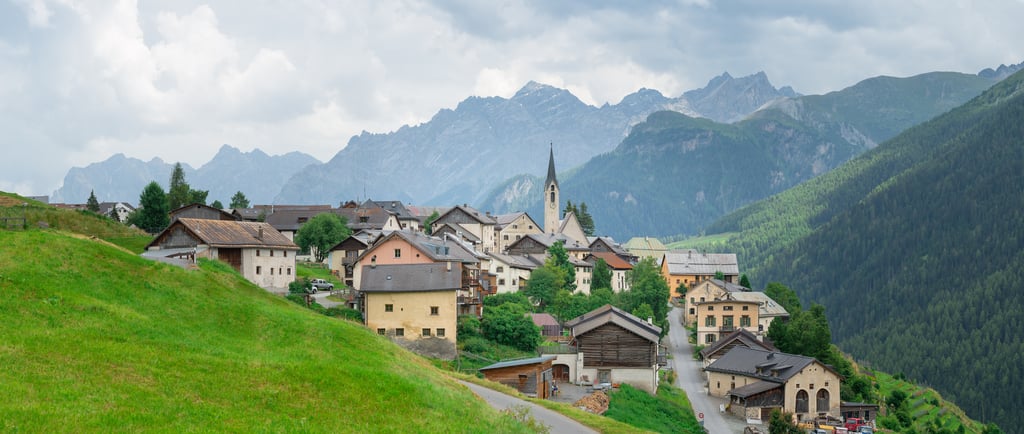Panoramic view of a traditional Swiss mountain village in the Alps with a church tower and green hills.