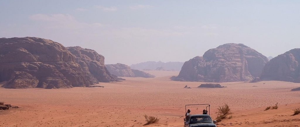 A 4x4 jeep safari tour driving through the red sand dunes and rock formations of Wadi Rum desert in Jordan.