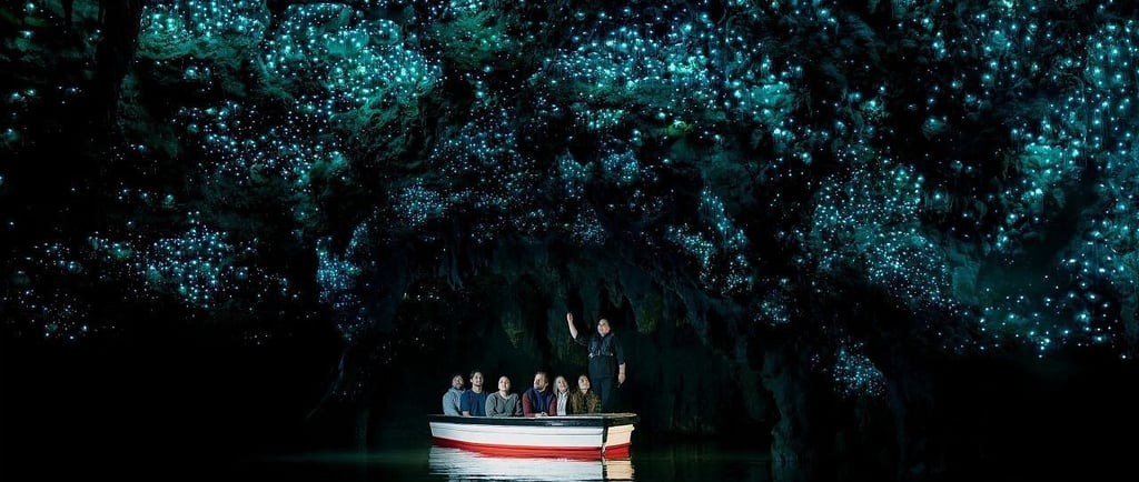 Tourists on a boat ride underneath bioluminescent glowworms in a dark New Zealand cave.