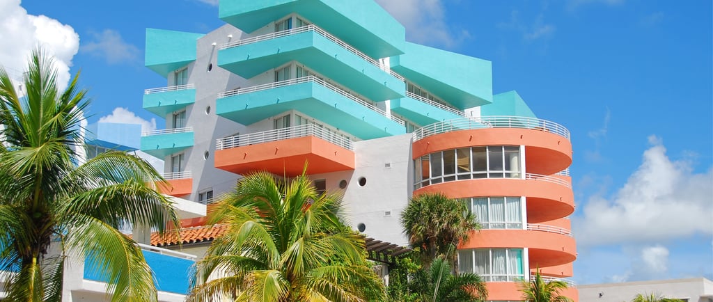 Colorful Art Deco hotel architecture in Miami Beach with teal and salmon balconies and palm trees.