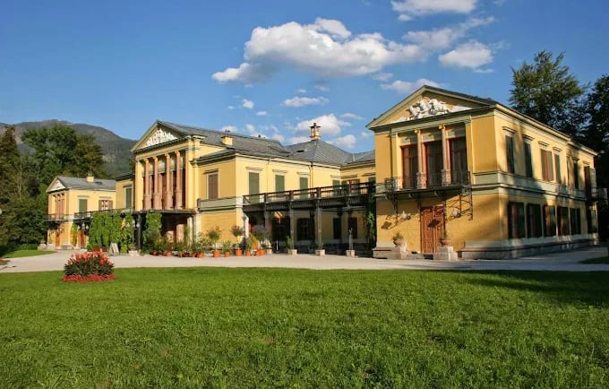 Yellow neoclassical imperial villa architecture with a green lawn and blue sky in Bad Ischl, Austria.