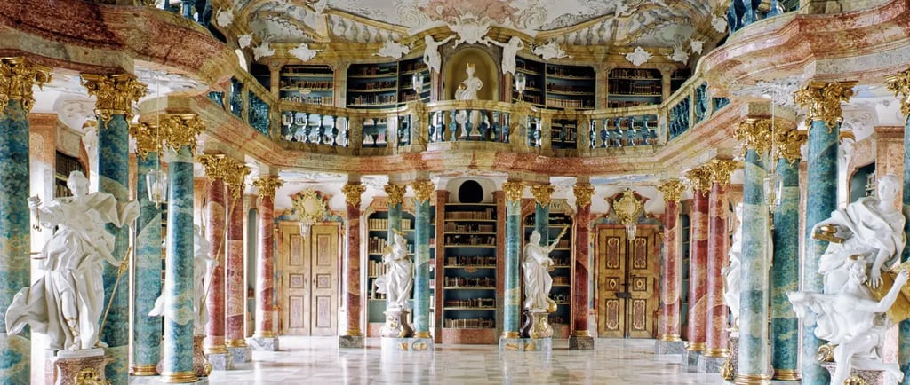 Ornate Baroque library interior with marble columns, gold accents, white statues, and historic books.