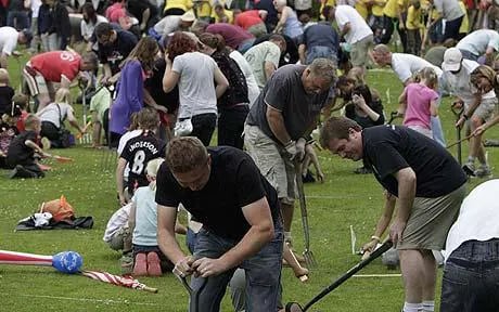 A large group of people participate in a worm charming competition on a grassy field.