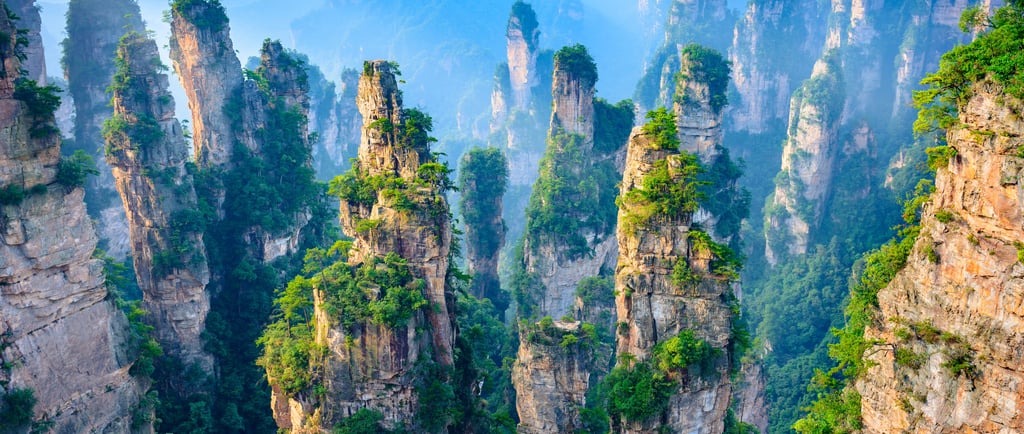 Aerial view of Zhangjiajie National Forest Park's tall sandstone pillars covered in green foliage and mist.