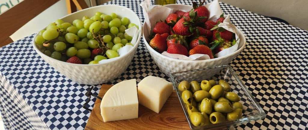 Fresh appetizers with green grapes, strawberries, olives, and cheese on a blue checkered tablecloth.