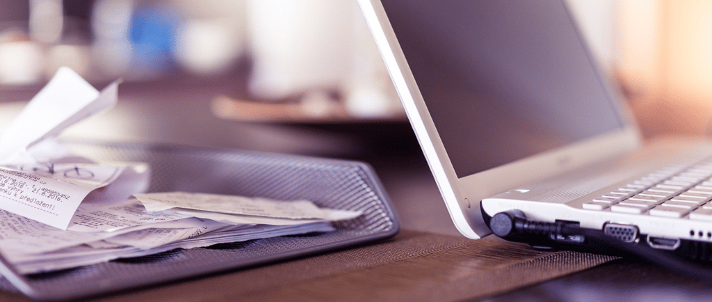 a laptop computer sitting on a desk with a stack of papers