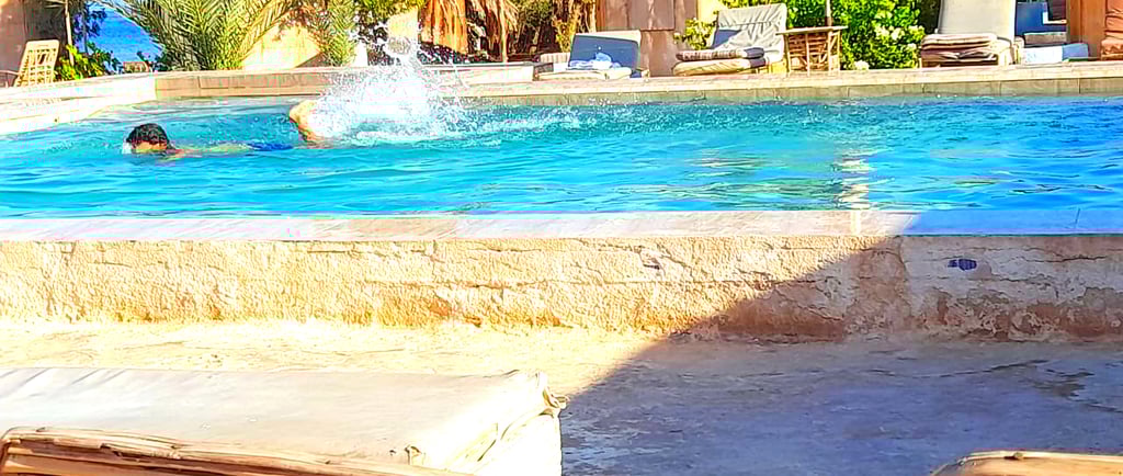 Niño nadando en la piscina cerca del mar y bungalow en Bedouin Star Egipto