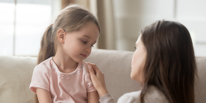 a woman in a pink shirt is resting her hand on a little girl's shoulder