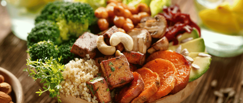 A colourful plate of avocado, sweet potato, broccoli, tofu, nuts, mushrooms, chickpeas and herbs