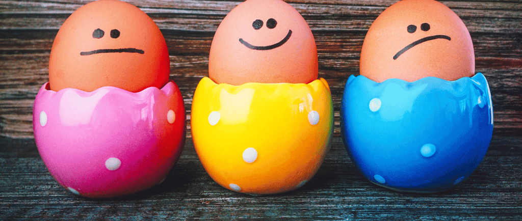 neutral, happy, sad face drawn on eggs in colourful egg cups