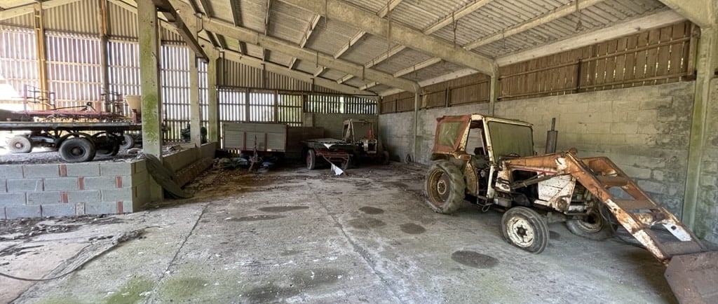 the inside of a large barn with rusting old tractors and farm machinery