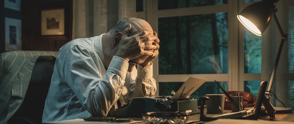 Fotografía de un hombre frente a una máquina de escribir, cogiéndose la cabeza perturbado.