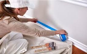 una chica con ropa para pintar pone cinta de enmascarar antes de pintar una pared