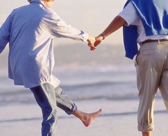 um homem e uma mulher de mãos dadas e caminhando na praia