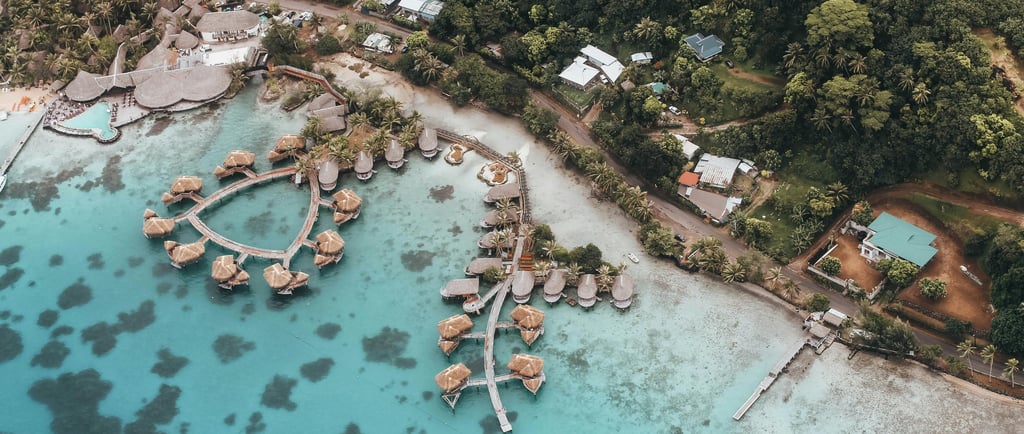 Aerial view of a coastal resort with overwater bungalows, surrounded by clear turquoise water