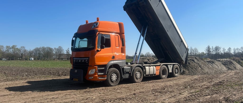 a dump truck with a dumpster sitting on the side of a dirt road