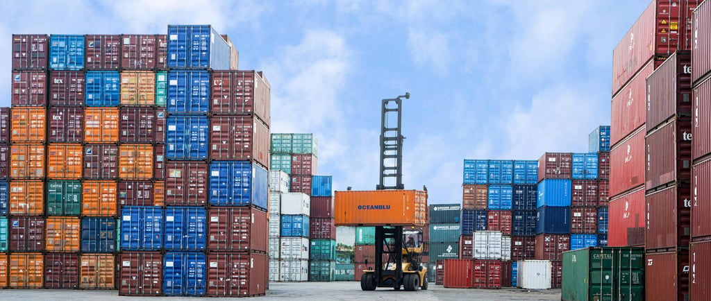 A forklift lifting a shipping container in a busy logistics terminal yard.
