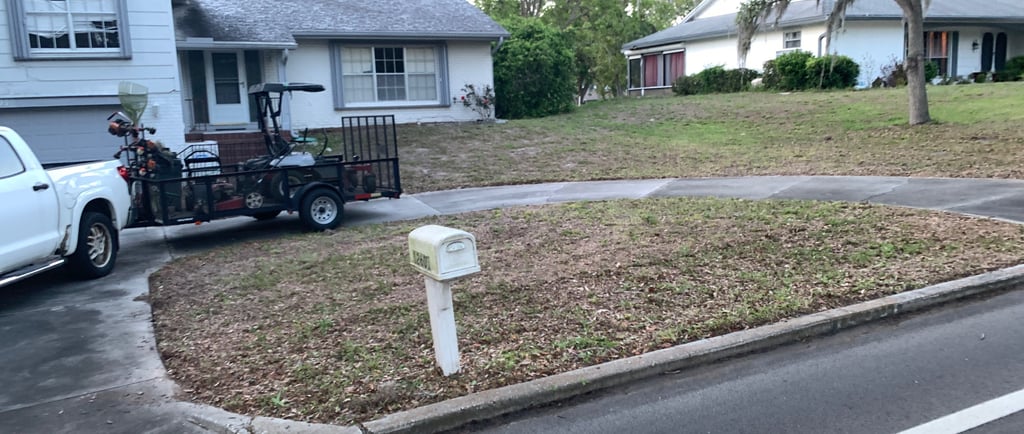 A white pickup truck with a landscaping trailer parked on a driveway in a residential neighborhood.