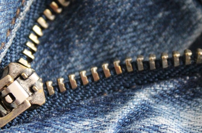 Close-up of a partially unzipped metal zipper on blue denim jeans.