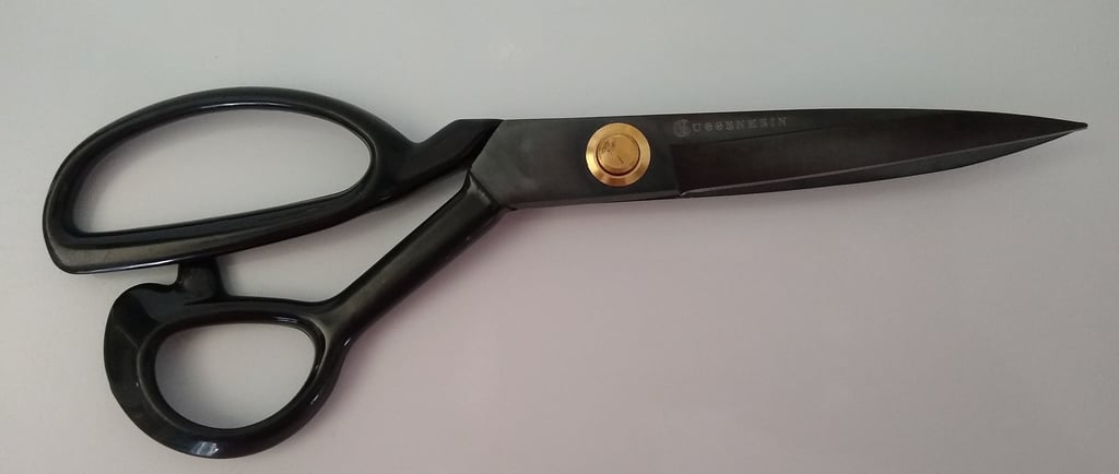 A pair of black Guggenhein sewing scissors with gold screw detail on a white background.