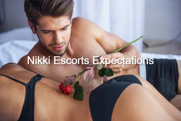 A handsome man lying in bed holding a red rose over a woman, illustrating Nikki Escorts expectations.