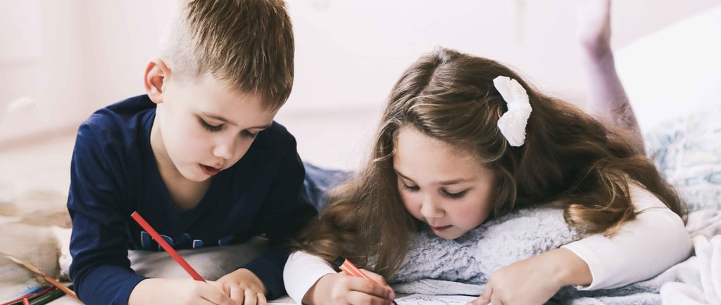 A girl and a boy are colouring in a colouring book whilst lying on the floor
