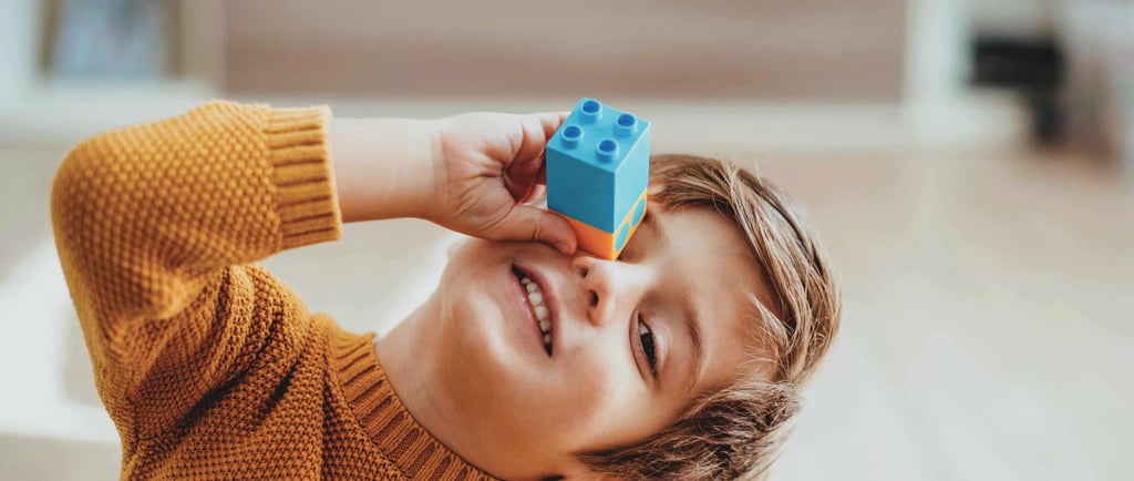 Smiling child holding a block to their eye.