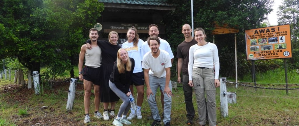A group of hikers posing at the entrance sign of Deramakot Forest Reserve in Sabah, Malaysia.