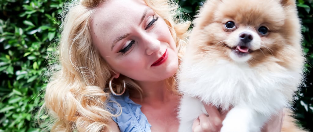 Founder of Liebe Chronicles holding Liebe, a dapper toy pomeranian, in a lush garden setting