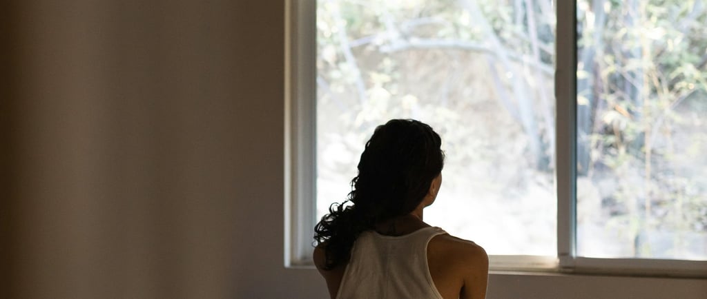 /a-woman-sitting-on-a-bed-looking-out-a-window