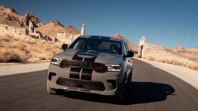 A grey Dodge Durango SRT Hellcat with racing stripes driving past desert ruins.