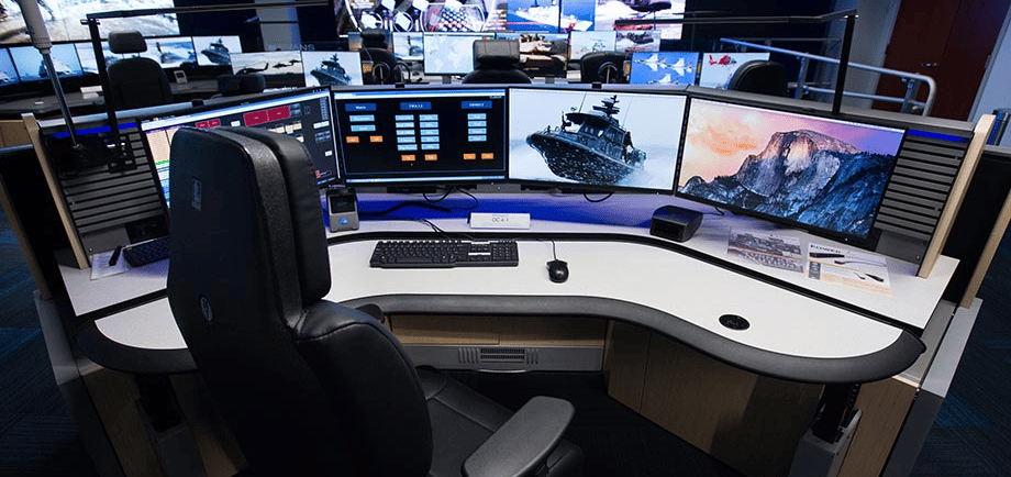 Security operations center workstation with multiple surveillance monitors and a large video wall.