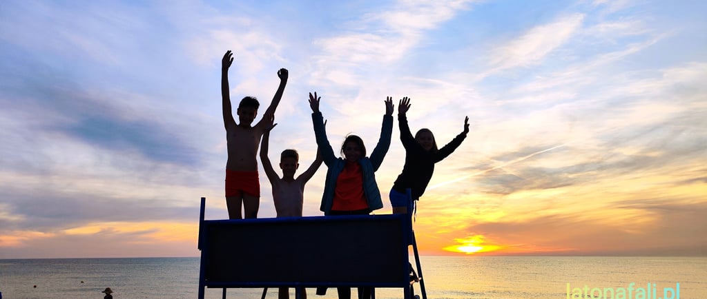 Rodzina w Dąbkach na plaży a w tle zachód słońca.