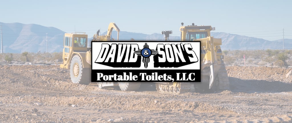 Heavy construction machinery at a desert work site with David and Son's Portable Toilets logo.