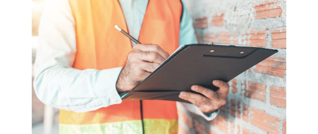 “Person wearing a reflective vest writing on a clipboard during a home inspection visit.”