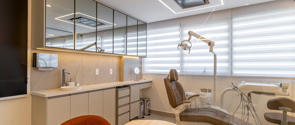 Consultório sofisticado com bancada de pedra clara, armários espelhados e cadeira odontológica.