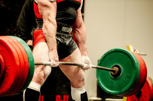 A muscular bodybuilder performing a heavy barbell deadlift during a powerlifting competition.