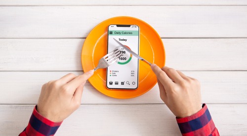 Person using a calorie counter app on a smartphone on a plate to track daily nutrition and diet.