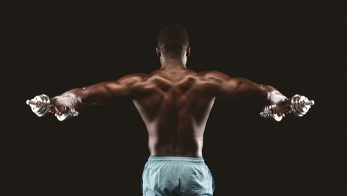 Back view of a muscular man performing lateral raises with dumbbells for shoulder strength training.